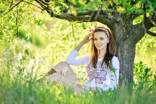 Bela jovem está sentado na grama no jardim — Fotografia de Stock