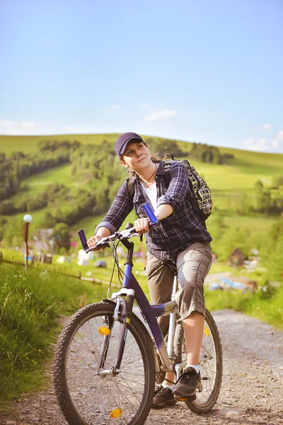 Jovem está viajando com uma bicicleta nas montanhas de verão — Fotografia de Stock