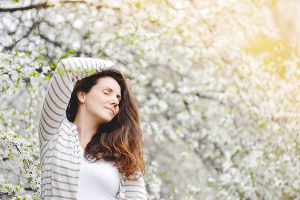 Jovem mulher fica perto de uma árvore florescente em um parque de primavera . — Fotografia de Stock