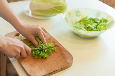 Bir salata kesme yaprakların bir ahşap tahta üzerinde bir kadındır.
