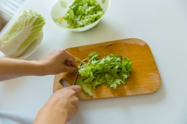 Bir salata kesme yaprakların bir ahşap tahta üzerinde bir kadındır.