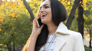 Genç, güzel esmer kadın sokakta bir ağacın yanında duruyor ve telefonla konuşuyor..