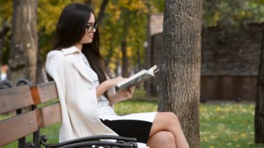 Güzel, genç bir esmer bankta oturuyor ve sabahları parkta kitap okuyor..