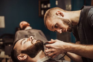 Profesyonel kuaför müşteri sakalı kesiyor.