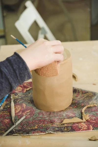 Child sculpts a small jar of wet clay