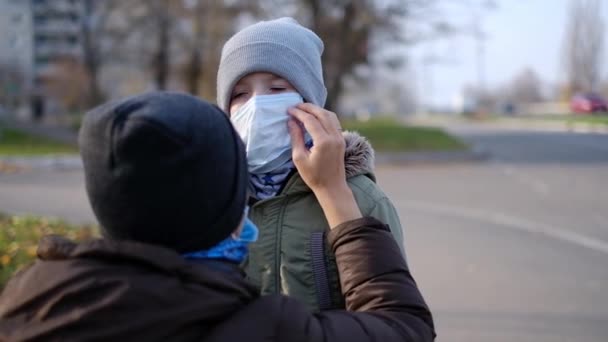 Kleine jongen in een medisch masker staat in de buurt van mam op straat. — Stockvideo