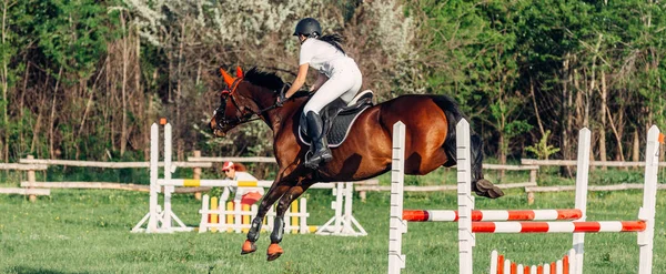 Une femme jockey saute une barrière sur un cheval dans les compétitions d'été . — Photo