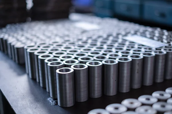 Metallzylinder stehen auf einem Tisch in der Nähe der Maschine in der Fabrik. viele runde Metallteile liegen auf dem Tisch. — Stockfoto