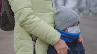 Bir Avrupa şehrinde Çin koronavirüsüne karşı koruma. Annem sokaktaki küçük oğluna koruyucu bir tıbbi maske takıyor..
