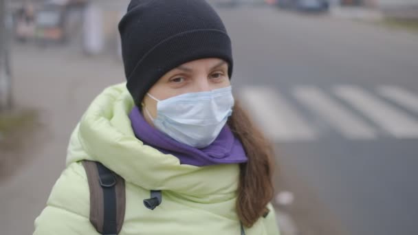 Skydd mot kinesiskt coronavirus i en europeisk stad. En ung kvinna på en offentlig plats står i en medicinsk mask i Tyskland. Uppkomst av symtom på coronavirus. — Stockvideo