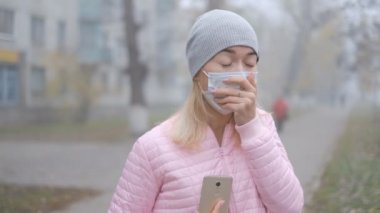 Coronavirus koruması. Tıbbi koruyucu maskeli genç bir kadın Avrupa 'da bir şehir caddesinde akıllı telefonuyla duruyor. Çin 'den gelen koronavirüsün belirtileri ortaya çıktı..