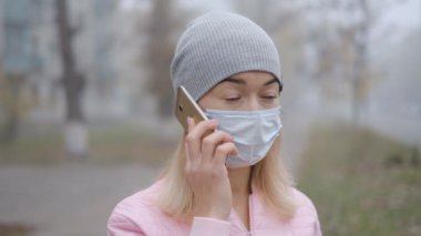Coronavirus koruması. Tıbbi koruyucu maskeli genç bir kadın Avrupa 'da bir şehir caddesinde akıllı telefonuyla duruyor. Çin 'den gelen koronavirüsün belirtileri ortaya çıktı..