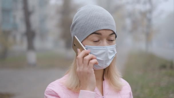 验尸官的保护 在欧洲的城市街道上 一个戴着医疗保护面具的年轻女子拿着智能手机站在那里 中国人出现了头孢病毒的症状 — 图库视频影像