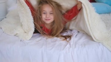 Küçük neşeli bir kız yorganın altından fırlıyor..