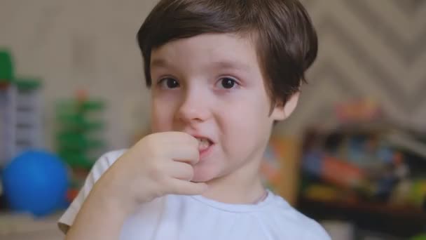 小さな男の子が子供部屋に立って、指をミルクの歯で振る。男の子は乳の歯を口から抜いて驚く。. — ストック動画
