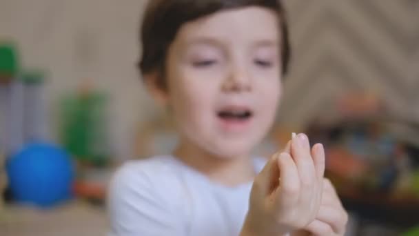 Ein kleiner Junge steht in einem Kinderzimmer und schüttelt mit den Fingern einen Milchzahn. zieht der Junge einen Milchzahn aus dem Mund und ist überrascht. — Stockvideo