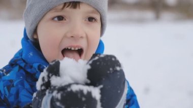 Çocuk kar yiyor, diliyle deniyor. Küçük çocuk kışın parkta yürür..