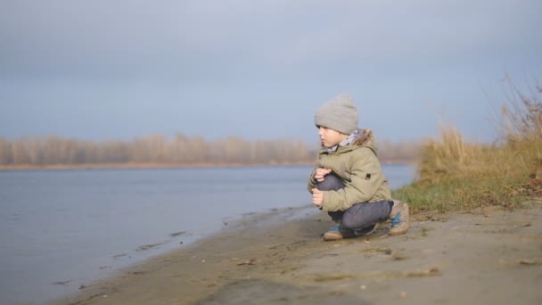 Мальчик осенью гуляет у реки. — стоковое видео