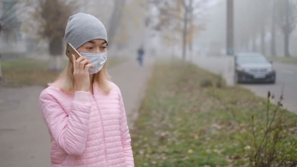 コロナウイルス対策 医療用保護マスクの若い女性がヨーロッパの街の通りにスマートフォンで立っています コロナウイルスの症状が現れました — ストック動画