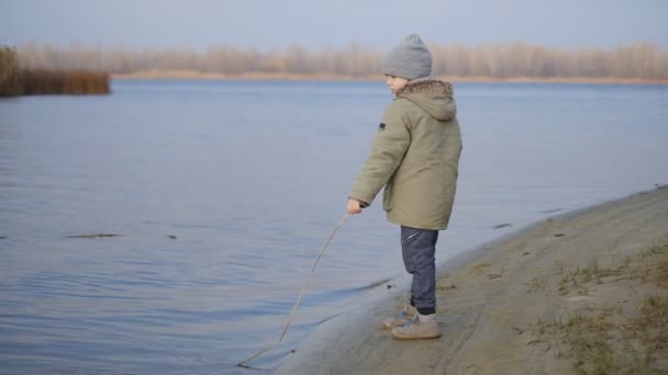 Ένα μικρό αγόρι περπατά κοντά στο ποτάμι το φθινόπωρο. — Αρχείο Βίντεο