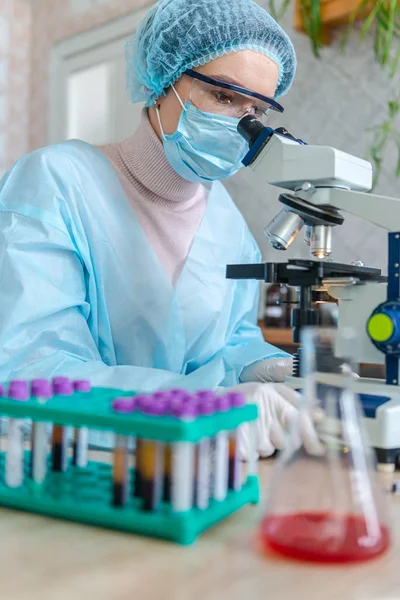 Female scientist studying coronavirus. The doctor looks through a microscope at a vaccine against coronavirus. — Stock Photo, Image