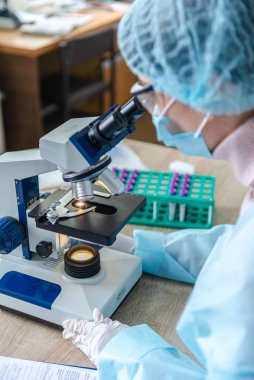 Koronavirüs üzerinde çalışan kadın bilim adamı. Doktor, koronavirüse karşı yapılan aşıyı mikroskopla inceliyor. Bir aşı oluşturuluyor.
