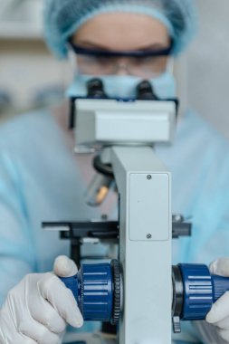 Koronavirüs üzerinde çalışan kadın bilim adamı. Doktor, koronavirüse karşı yapılan aşıyı mikroskopla inceliyor. Bir aşı oluşturuluyor.