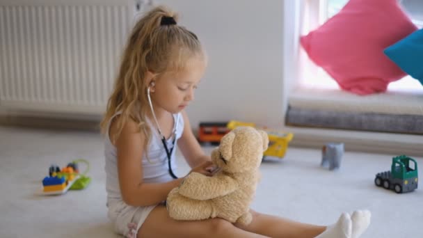 Uma menina está brincando de médico com seu urso de brinquedo . — Vídeo de Stock