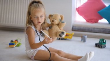 Küçük bir kız oyuncak ayısıyla doktorculuk oynuyor..