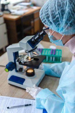 Koronavirüs üzerinde çalışan kadın bilim adamı. Doktor, koronavirüse karşı yapılan aşıyı mikroskopla inceliyor. Bir aşı oluşturuluyor.