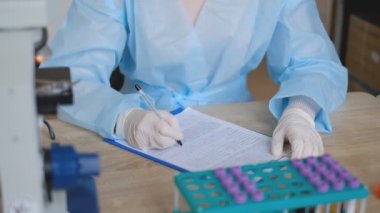 Doktor laboratuarda araştırma yürütüyor. Bir belgeye bilgi yazar. Kadın bir bilim adamı koronavirüs çalışmalarının sonuçlarını kaydediyor..