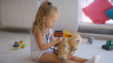 Küçük bir kız oyuncak ayısıyla doktorculuk oynuyor..