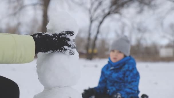 冬の公園で小さな息子を持つお母さんは雪だるまを彫刻します. — ストック動画