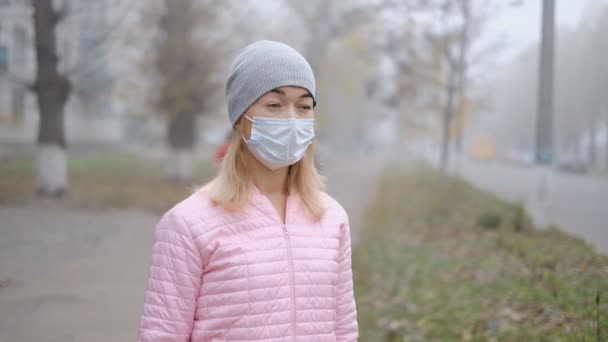 Skydd mot kinesiskt coronavirus i en europeisk stad. En ung kvinna på en offentlig plats står i en medicinsk mask i Tyskland. Uppkomst av symtom på coronavirus. — Stockvideo