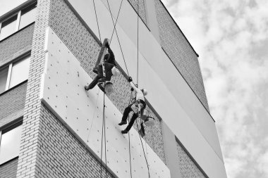 İki profesyonel adam dışarıdaki bir binayı izole ediyor. Endüstriyel yükseklik. İki dağcı evin duvarını iplerle yalıtıyor..