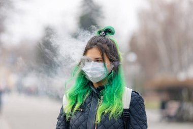 Yeşil saçlı, koruyucu bir maske takan ve sigara içen bir kız..