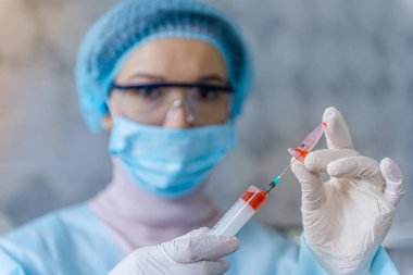 Bir doktor koronavirüse karşı aşı yapmaya hazırlanıyor. Doktor şırıngaya bir ilaç enjekte ediyor..