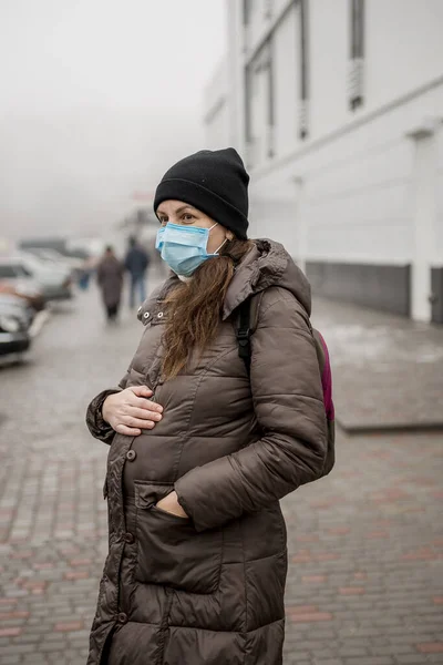 Tıbbi maskeli hamile bir kadın Almanya 'da bir caddede duruyor. Hamile bir kadın, koronavirüs salgını sırasında bir Avrupa şehrinin caddesinde duruyor..