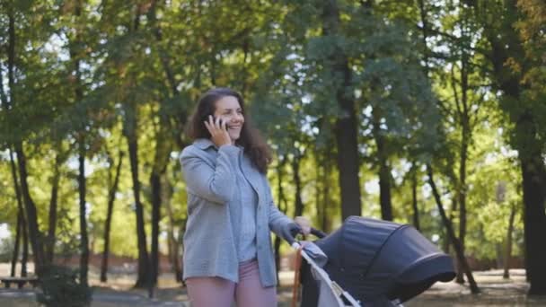 Une jeune mère marche dans le parc avec un bébé endormi dans un landau . — Video