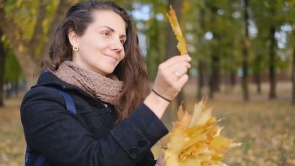 Sarı sonbahar yapraklarını elinde tutan genç bir kadın.. — Stok video