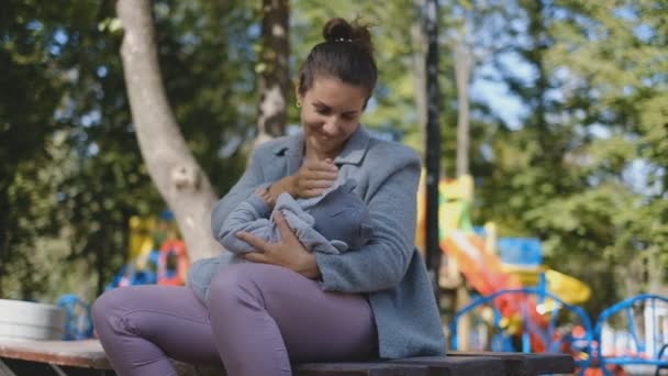 Uma mulher está amamentando seu bebê ao ar livre em um parque . — Vídeo de Stock