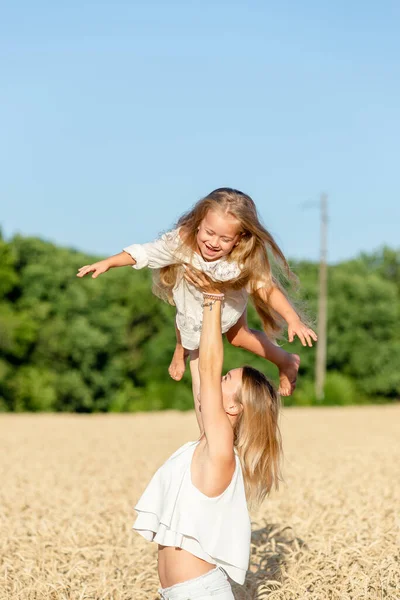 Eine junge Frau steht im Sommer in einem Weizenfeld und hält ihre kleine Tochter im Arm. — Stockfoto