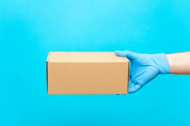 Bir adam elinde lastik eldiven olan bir karton kutu tutuyor. COVID-19 'a karşı koruma. Coronavirüs salgını sırasında malların güvenli bir şekilde teslim edilmesi..
