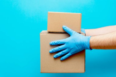 Bir adam elinde lastik eldiven olan bir karton kutu tutuyor. COVID-19 'a karşı koruma. Coronavirüs salgını sırasında malların güvenli bir şekilde teslim edilmesi..