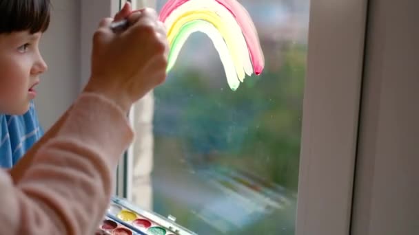 De jacht op de regenboog. Een jongetje tekent een regenboog op een quarantainevenster. Pandemische covid-19 . — Stockvideo