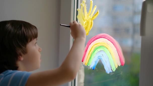 De jacht op de regenboog. Een jongetje tekent een regenboog op een quarantainevenster. Pandemische covid-19 . — Stockvideo