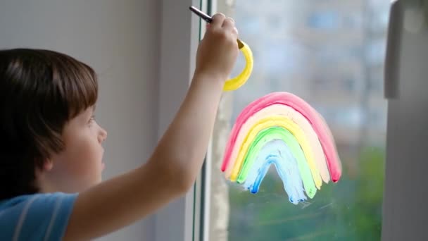 La persecución del arco iris. Un niño pequeño dibuja un arco iris en una ventana de cuarentena. Covidio pandémico-19  . — Vídeos de Stock