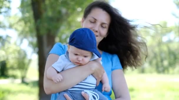 Matka s novorozeným batoletem sedí na jaře v parku. Projdi se s batoletem v parku. Izolace od lidí na procházce s novorozencem během epidemie KOVID-19. — Stock video