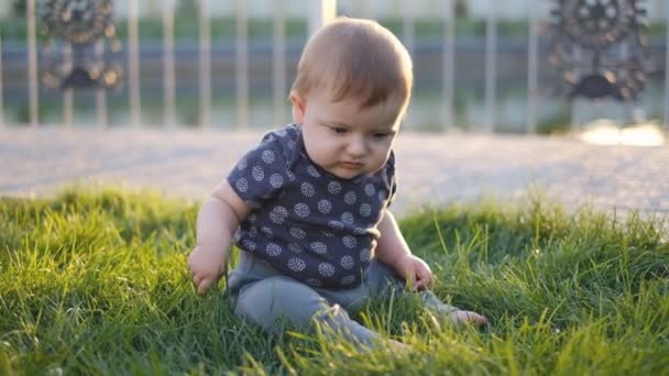 El niño pequeño está sentado sobre hierba fresca y verde en el parque de primavera. Un niño pequeño camina en el parque durante una pandemia . — Vídeos de Stock