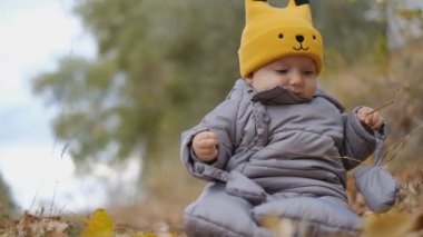 Küçükler sonbaharda parkta sarı yaprakların içinde otururlar. Bebekle sonbahar yürüyüşü. Sarı sonbahar yaprakları olan bir çocuk..